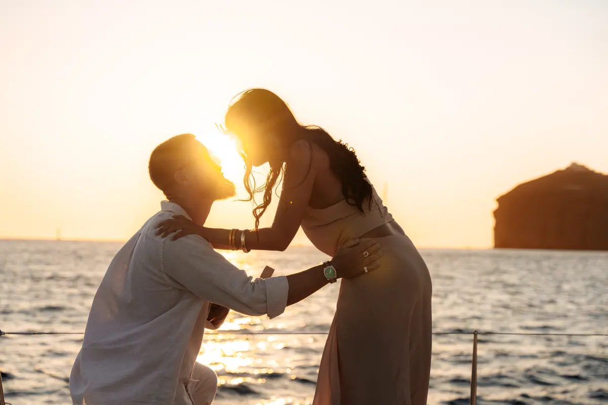 A proposal on the foredeck: one guest on one knee, both of them backlit by the setting sun.