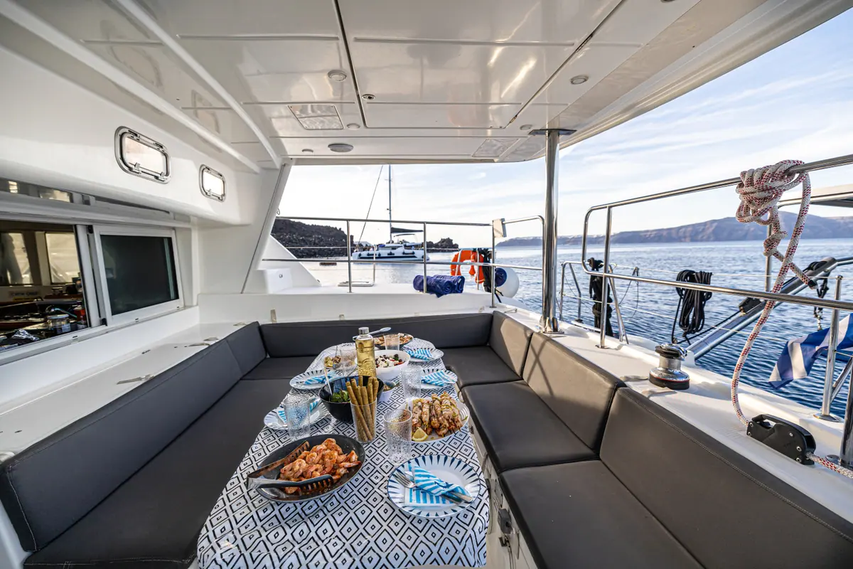 The cockpit table laid for the evening meal — bread, cheese, olives and skewers — with the sea past the rail.