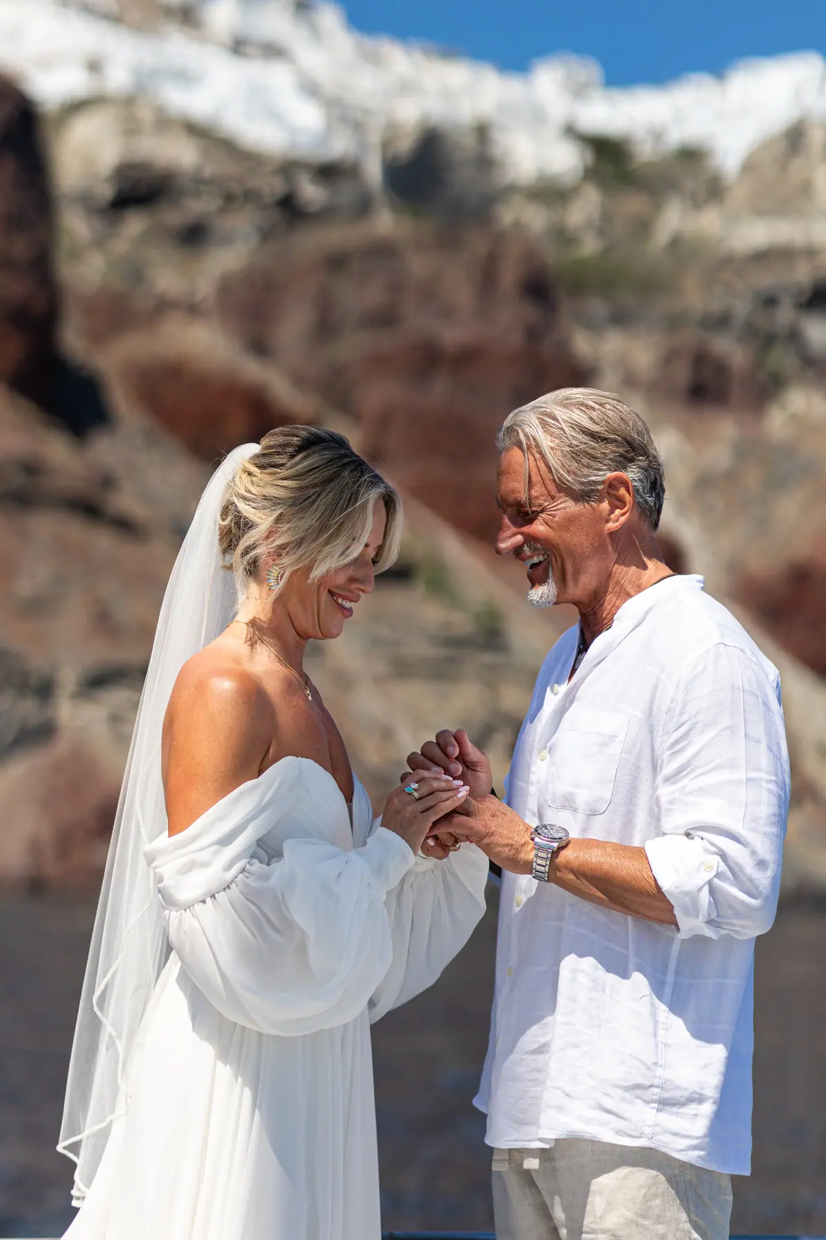 A newly married couple hand in hand at the bow, the caldera cliff behind them.