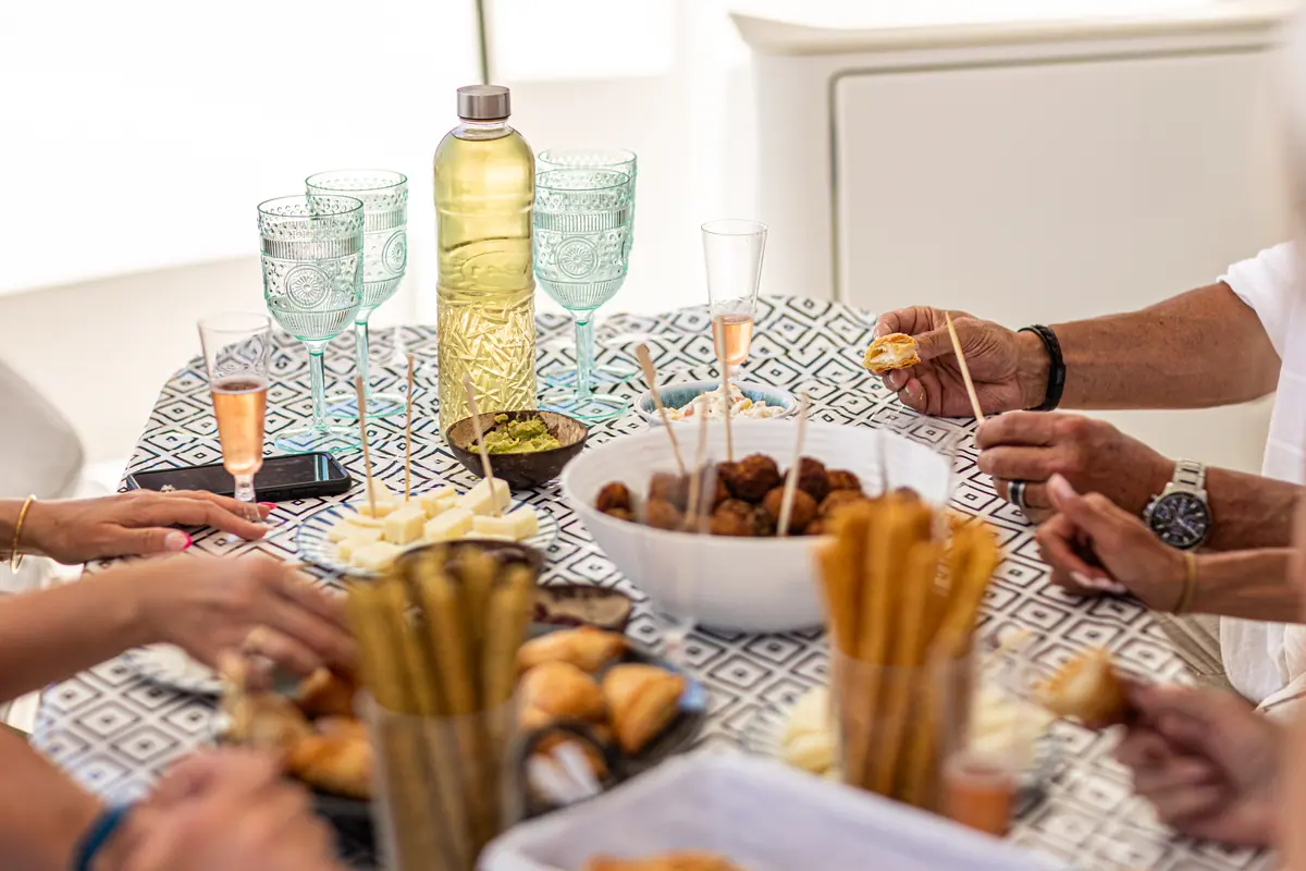 Several pairs of hands reaching across the cockpit table for bread, olives and cheese.