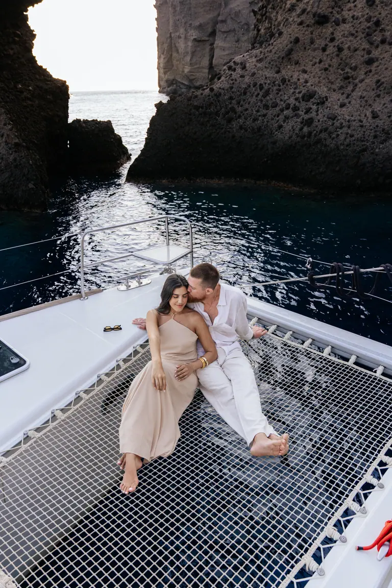 A couple lying together on the catamaran’s forward trampolines above deep blue water.