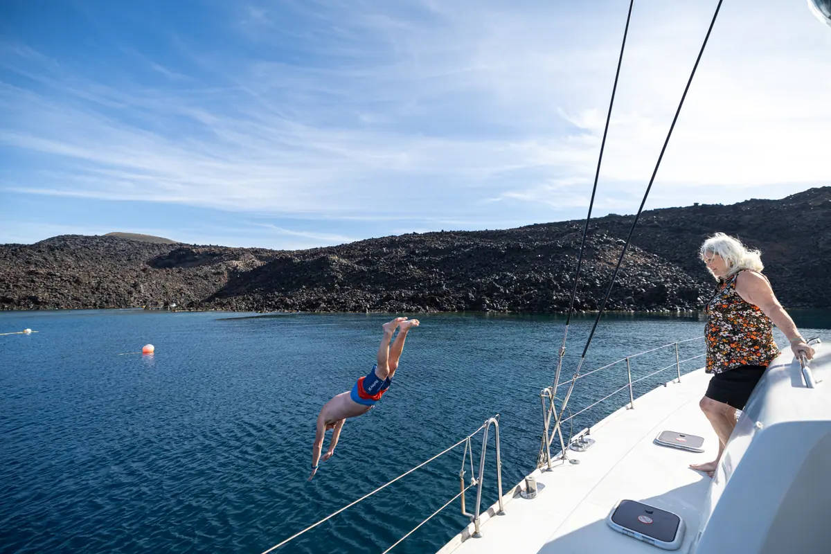 A guest standing on the foredeck as the boat lies off the dark lava shore of the volcano.