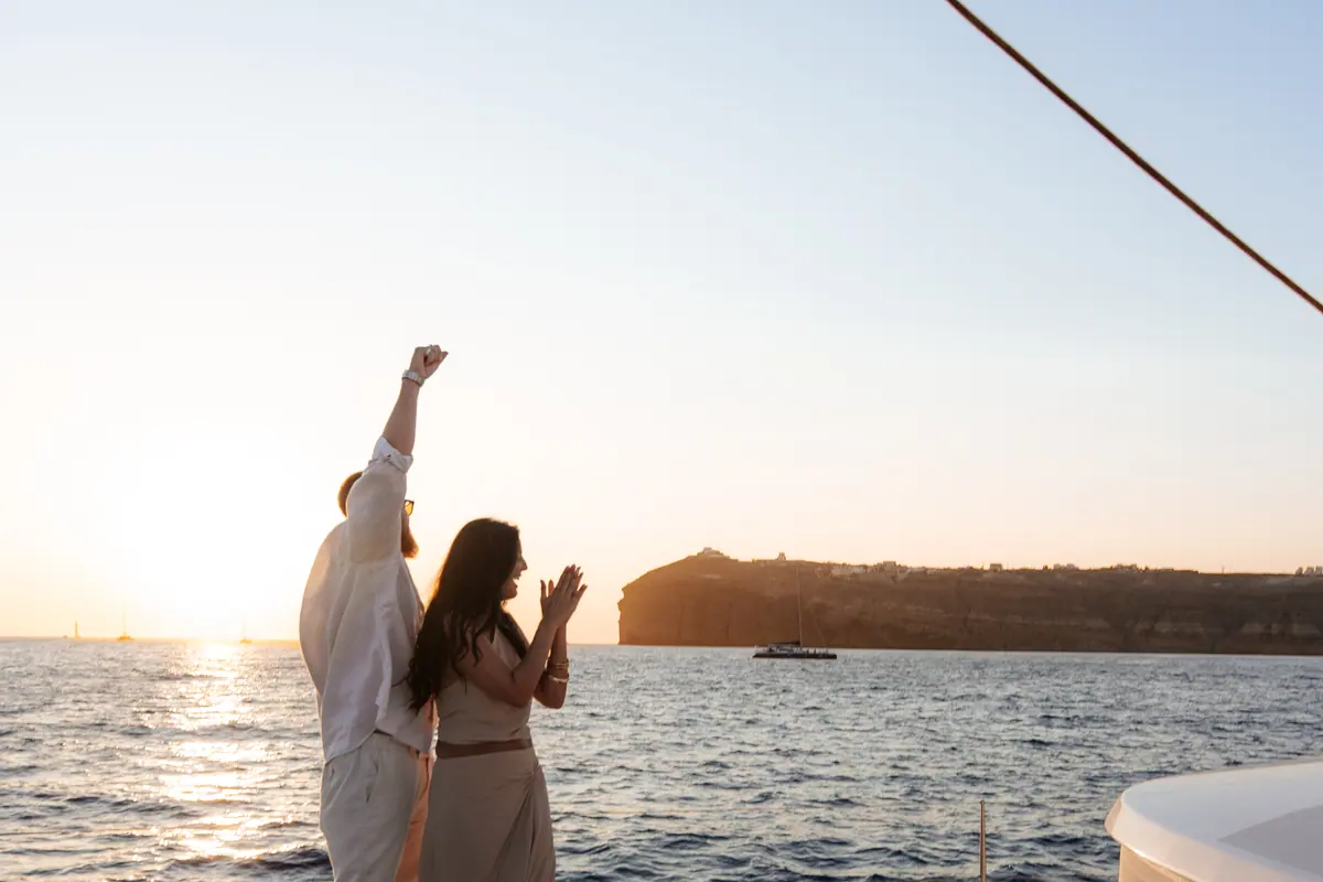 Two guests celebrating at the rail as the sun drops to the horizon.