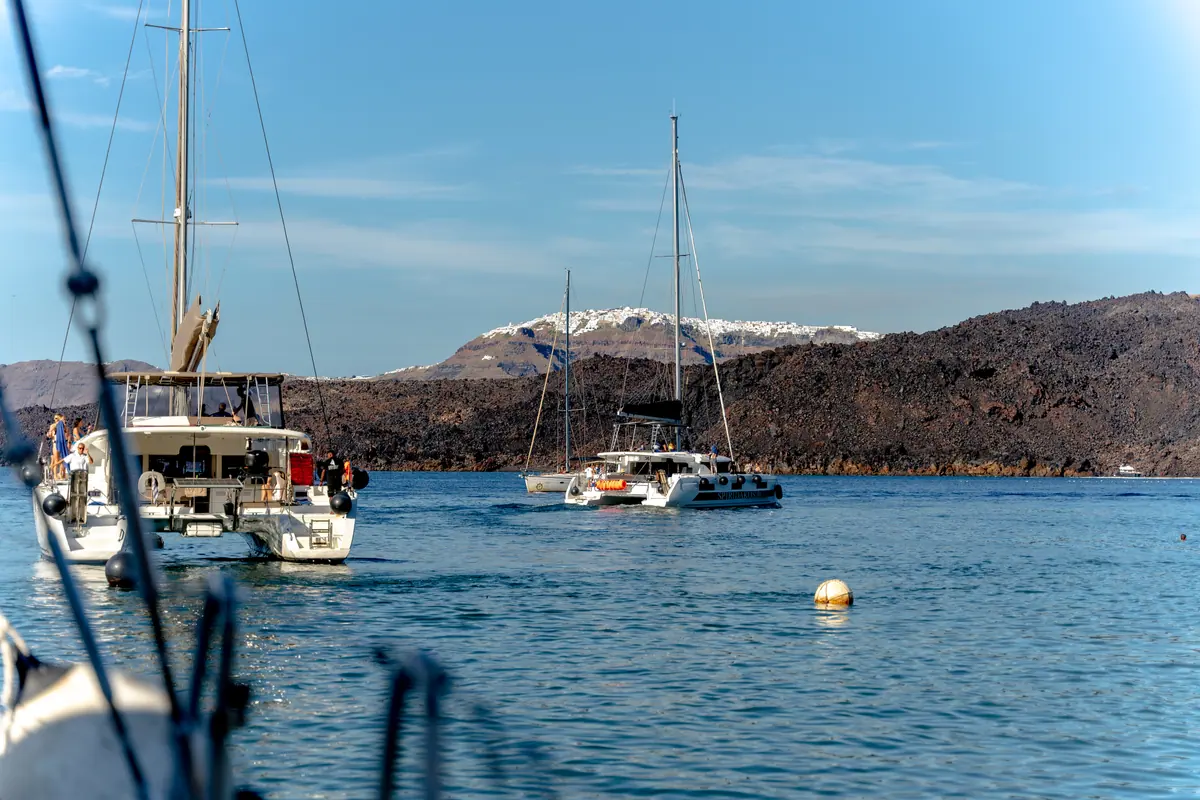 The black lava shore of Nea Kameni dropping straight into the water, with the white villages on the caldera rim behind it.